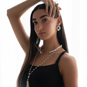 Woman wearing a black top and pearl necklace and earrings on a white background