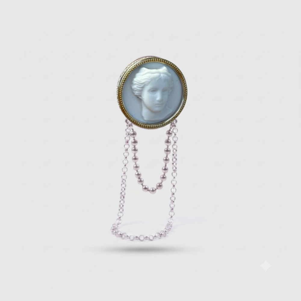 A vintage-style pendant brooch featuring a circular gold-toned frame with a white carved classical bust, suspended from a delicate dangling chain, shown on a light gray background.