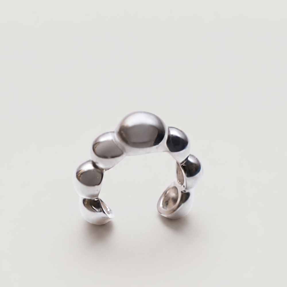 A polished silver cuff with a unique segmented, pebble-like design, photographed on a clean, light off-white background.