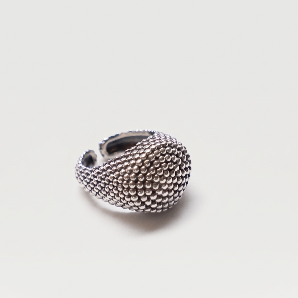 A textured silver ring with a unique teardrop-shaped, beaded surface, photographed on a clean, light gray background.