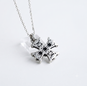 A silver cross pendant necklace with intricate cutout detailing, hanging from a delicate silver chain against a clean white background.