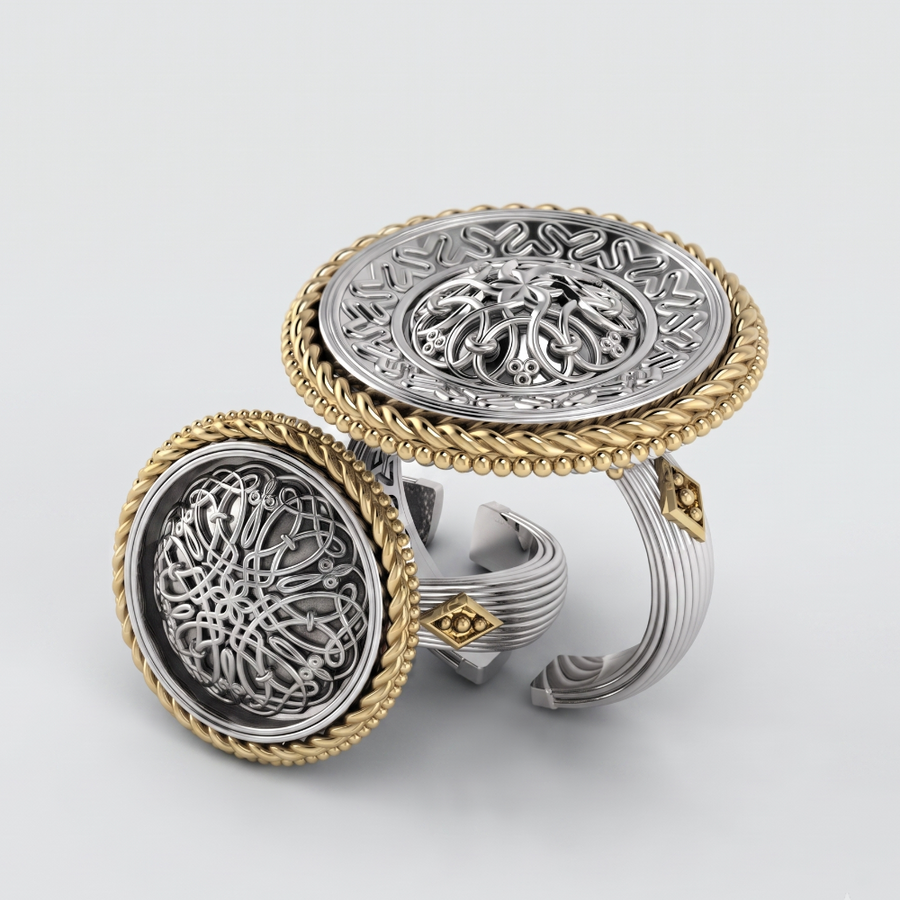 A pair of ornate two-tone rings with intricate filigree and Arabic calligraphy designs, featuring silver-toned centers, gold-toned rope borders, and a textured wrap-around shank, shown on a light gray background.