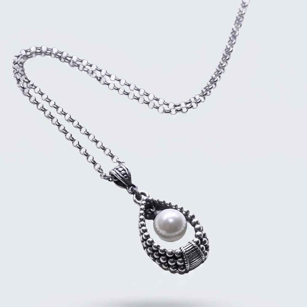 A silver-toned beaded chain necklace with a teardrop-shaped pendant featuring a central white pearl, shown on a light gray background.