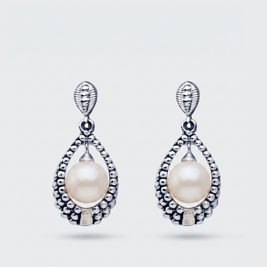 A pair of silver teardrop dangle earrings featuring a central white pearl surrounded by a textured beaded silver border, set against a light gray background.