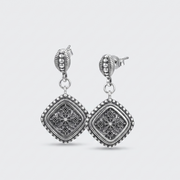 A pair of silver-toned drop earrings with square filigree charms, shown on a light gray background.