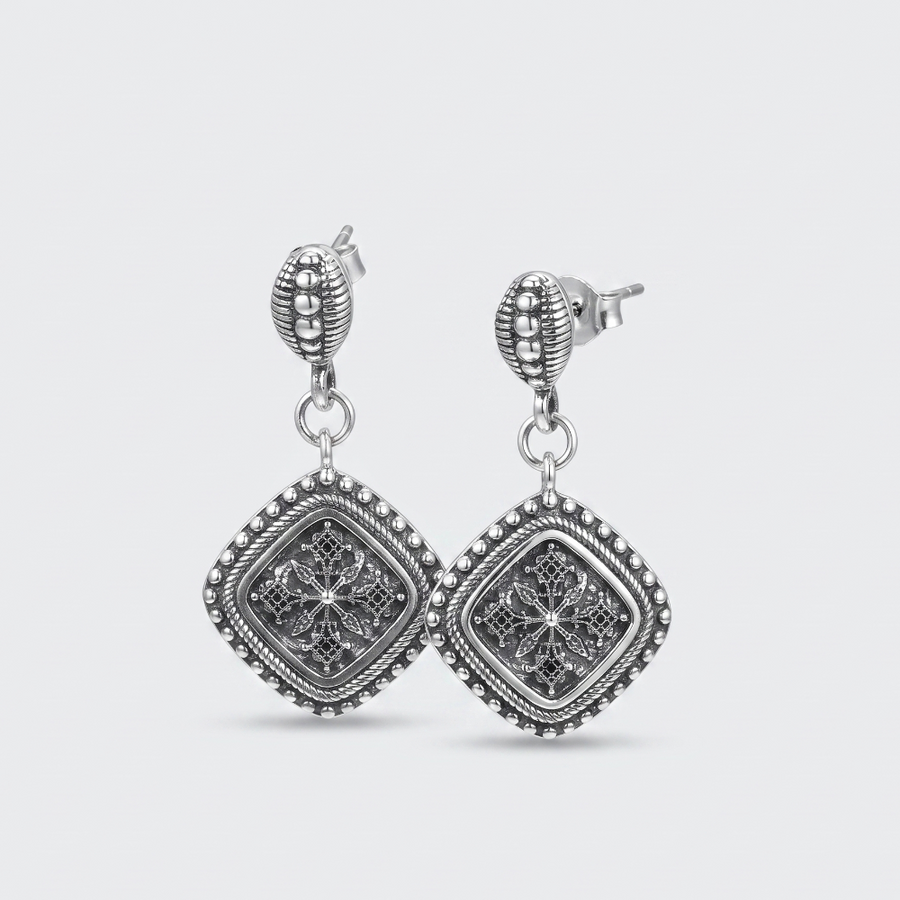 A pair of silver-toned drop earrings with square filigree charms, shown on a light gray background.