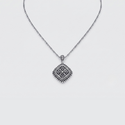 A silver necklace with a square pendant featuring a raised floral or starburst motif and a beaded border, shown on a light gray background.