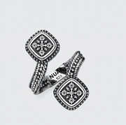 A pair of silver-toned cufflinks with square medallion faces, intricate geometric patterns, and twisted rope-like bands, displayed on a light gray background. One cufflink shows a 'NU 925' hallmark.