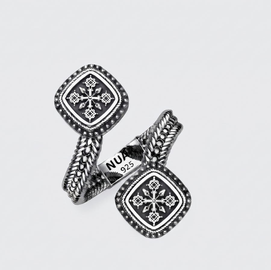 A pair of silver-toned cufflinks with square medallion faces, intricate geometric patterns, and twisted rope-like bands, displayed on a light gray background. One cufflink shows a 'NU 925' hallmark.