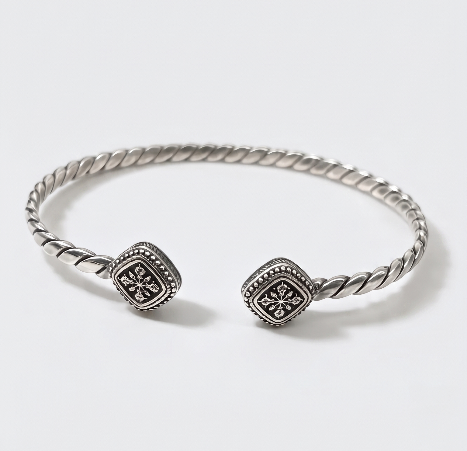A silver-toned twisted cable cuff bracelet with two square pavé-set bezel stones, photographed on a clean white background.