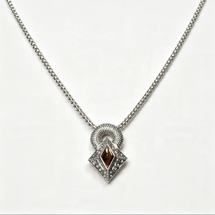 A silver-toned chain necklace with a geometric pendant featuring a central dark brown marquise-cut stone surrounded by small clear stones, set against a plain white background.
