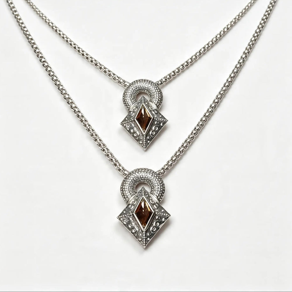 A pair of silver-tone layered necklaces with diamond-shaped pendants featuring dark brown gemstone centers and clear accent stones, displayed on a clean white background.