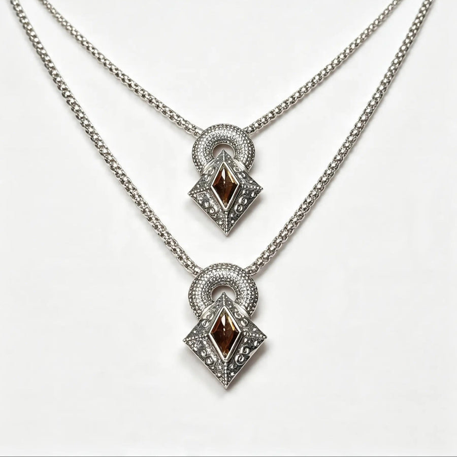 A pair of silver-tone layered necklaces with diamond-shaped pendants featuring dark brown gemstone centers and clear accent stones, displayed on a clean white background.
