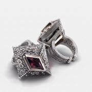A pair of silver-toned vintage-style ring stands with ornate beaded borders and a central rectangular red gemstone, photographed on a clean white background.