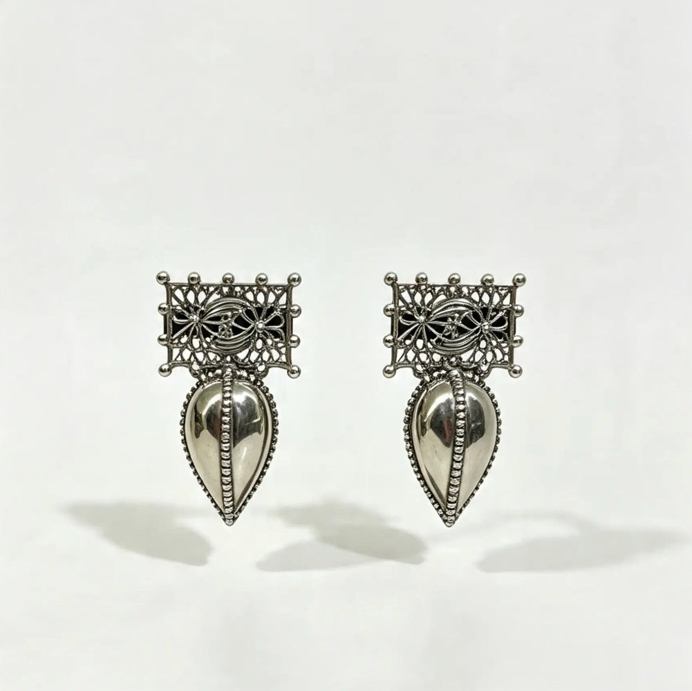 A pair of silver-toned traditional earrings with intricate filigree tops and teardrop-shaped dangling pendants, shown on a plain white background.