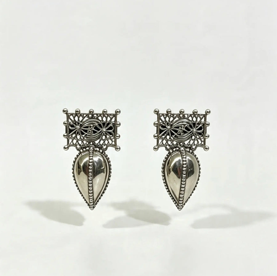 A pair of silver-toned traditional earrings with intricate filigree tops and teardrop-shaped dangling pendants, shown on a plain white background.