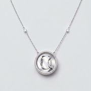 A silver pendant necklace featuring a circular bezel-set setting with a stylized letter 'Q' pendant, suspended from a delicate chain with two small accent beads on either side, set against a light gray background.