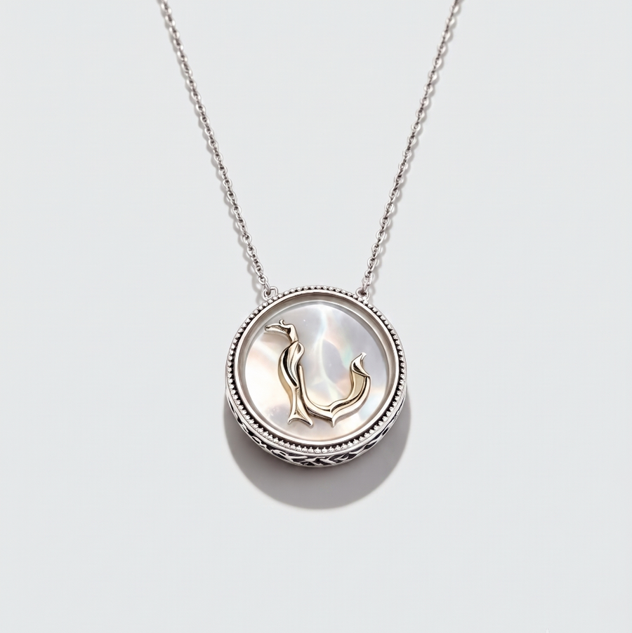 A silver pendant necklace featuring a circular bezel-set shell inlay with a small gold penguin motif, suspended from a delicate silver chain against a light gray background.