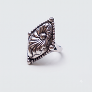 A silver ring featuring an ornate, textured floral or nautilus shell-like centerpiece with a beaded triangular border, shown on a plain light gray background.