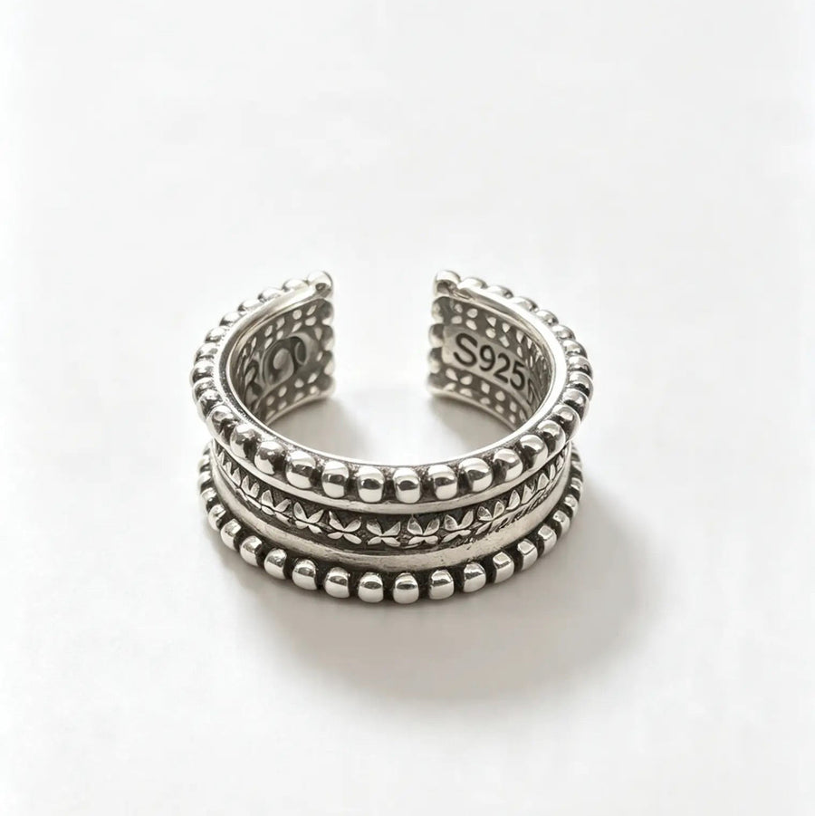 A silver-toned open cuff ring with three stacked textured bands featuring beaded edges and geometric patterns, photographed on a clean white background.