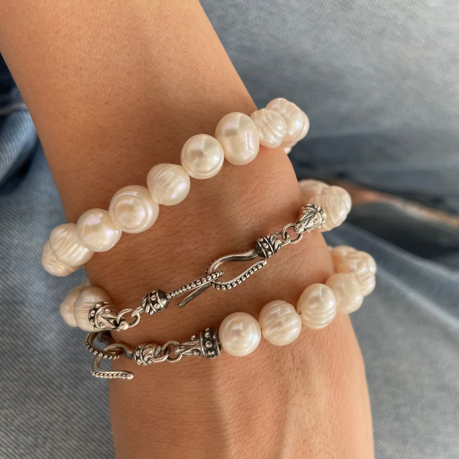 Three beaded bracelets on a person's wrist, featuring white pearl-like beads with textured details and silver-toned metal spacers and clasps, worn over light blue denim jeans.