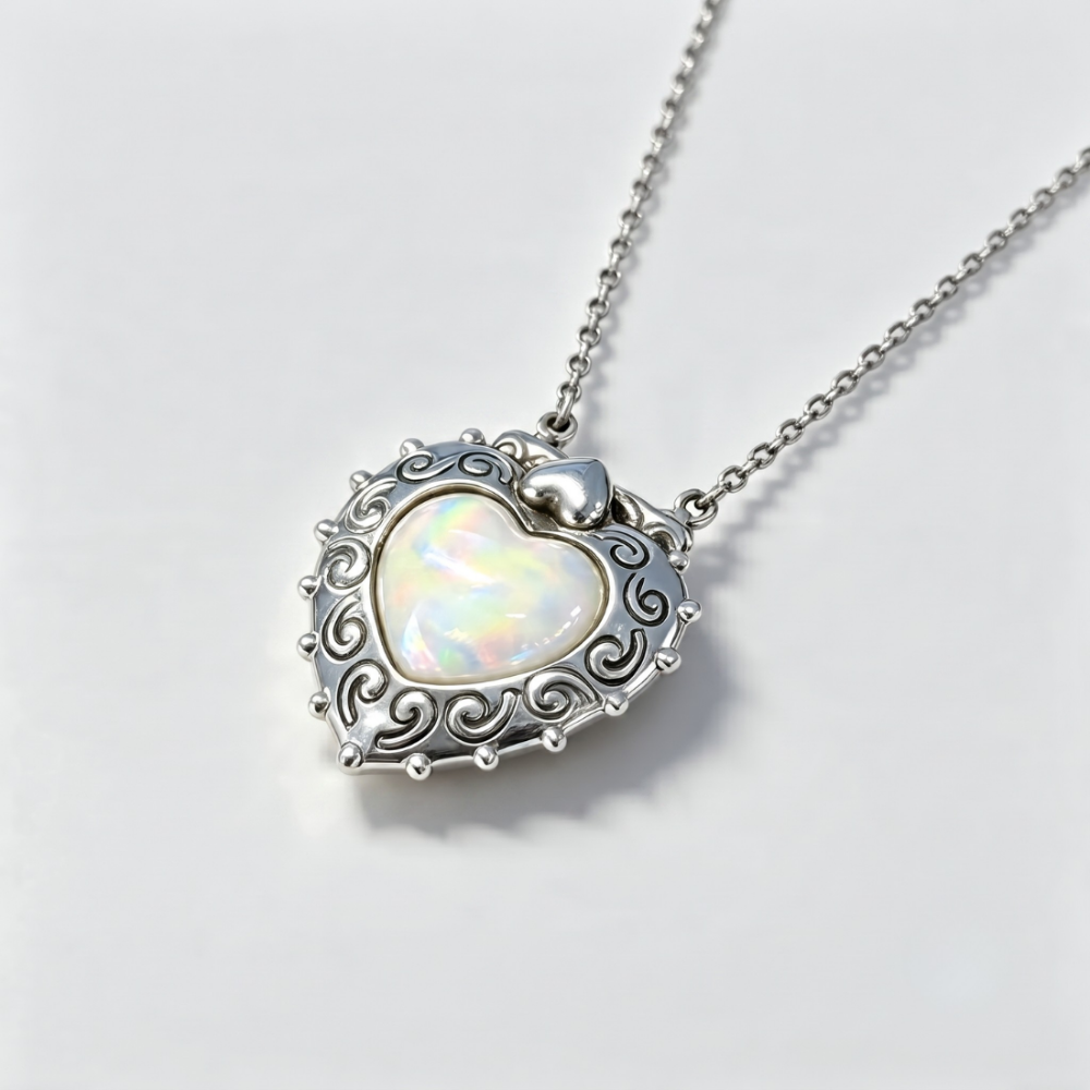 A silver heart-shaped pendant necklace with an iridescent white opal center and an ornate scrollwork border, shown on a clean white background.