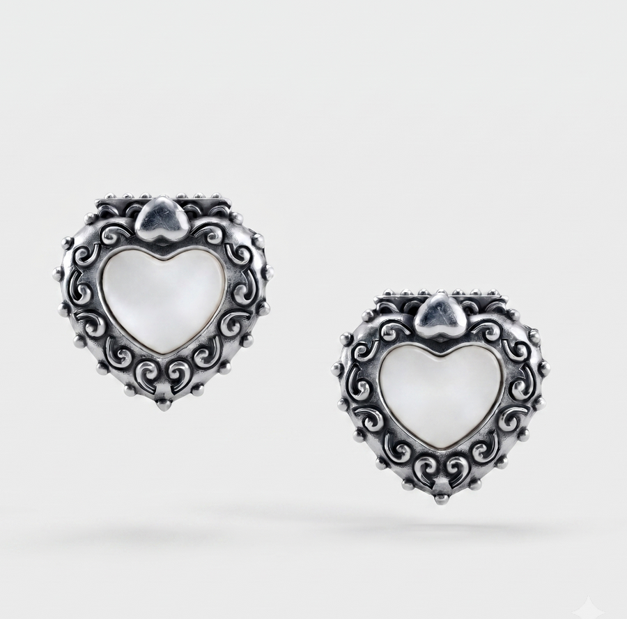 A pair of silver heart-shaped earrings with ornate scrollwork borders and white mother-of-pearl centers, shown on a light gray background.