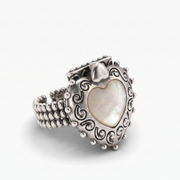 A silver heart-shaped ring featuring a central iridescent mother-of-pearl heart inlay, surrounded by ornate scrollwork and a beaded band, set against a plain light gray background.