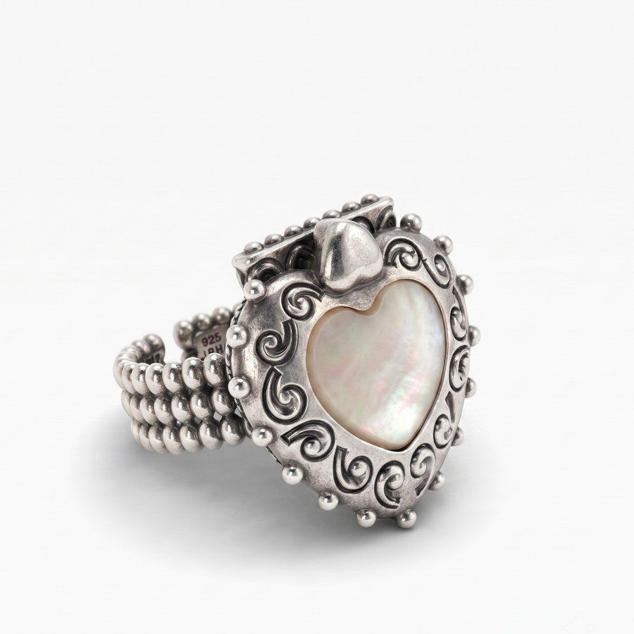 A silver heart-shaped ring featuring a central iridescent mother-of-pearl heart inlay, surrounded by ornate scrollwork and a beaded band, set against a plain light gray background.