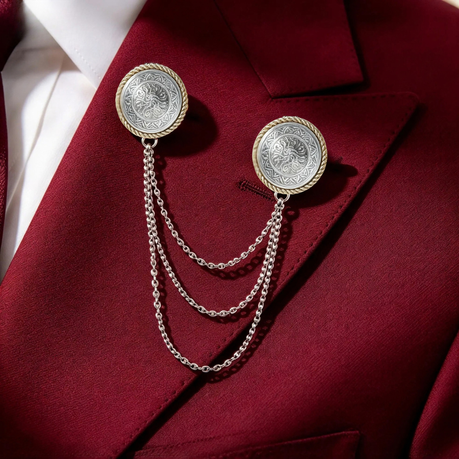 A men's formal accessory set featuring a silver-toned chain lapel pin with two round medallion pins, styled on a deep burgundy suit jacket over a white dress shirt.