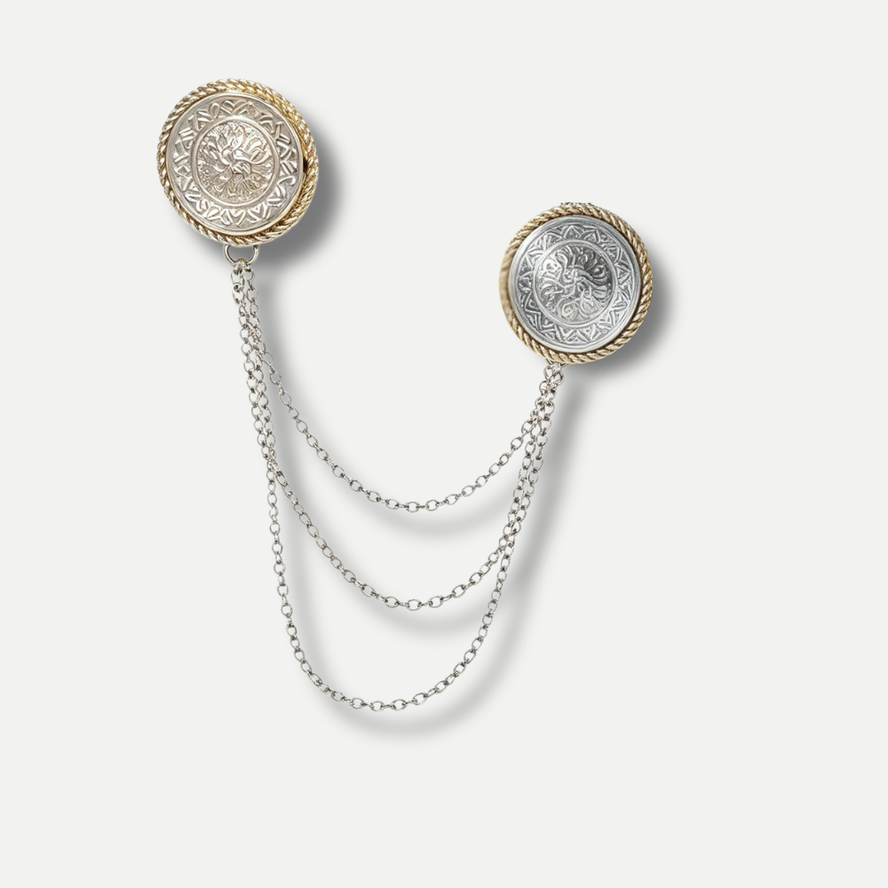 A vintage-style double earring brooch featuring two circular medallion studs with ornate floral engravings, one in gold and one in silver, connected by three draped silver chains on a light gray background.