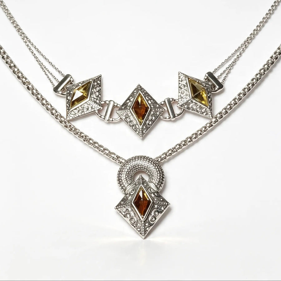A silver-tone double-strand necklace featuring three diamond-shaped motifs with amber-brown gemstones and clear crystals, with a matching pendant hanging below on a white background.
