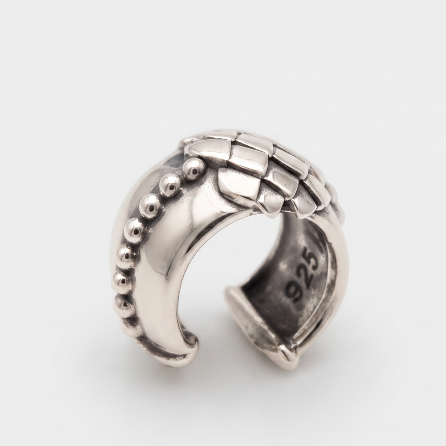 A sterling silver curved ring with a textured basketweave pattern on the top and a row of small raised beads on one side, photographed on a clean light gray background.