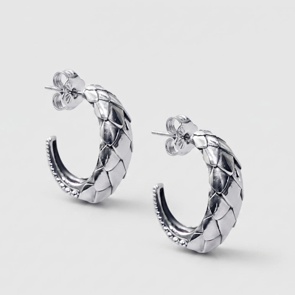 A pair of silver hoop earrings with a textured, woven or scaled pattern and post-back closures, shown on a light gray background.