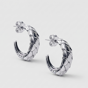 A pair of silver hoop earrings with a textured, woven or scaled pattern and post-back closures, shown on a light gray background.