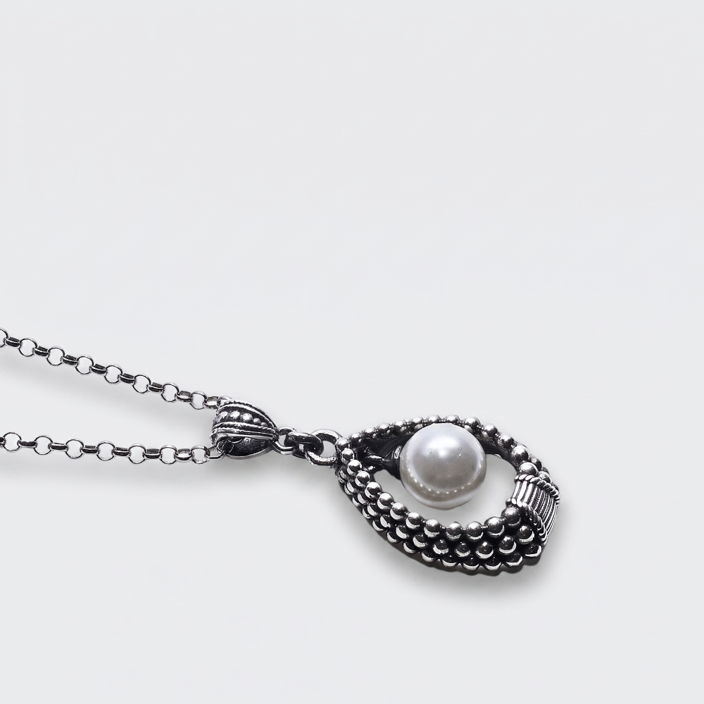 A silver-toned necklace with a textured, beaded teardrop-shaped pendant holding a single white pearl, shown on a light gray background.