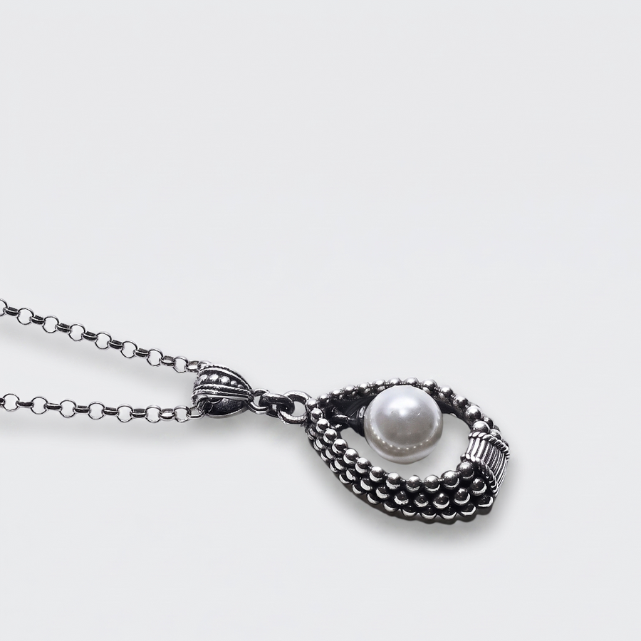 A silver-toned necklace with a textured, beaded teardrop-shaped pendant holding a single white pearl, shown on a light gray background.