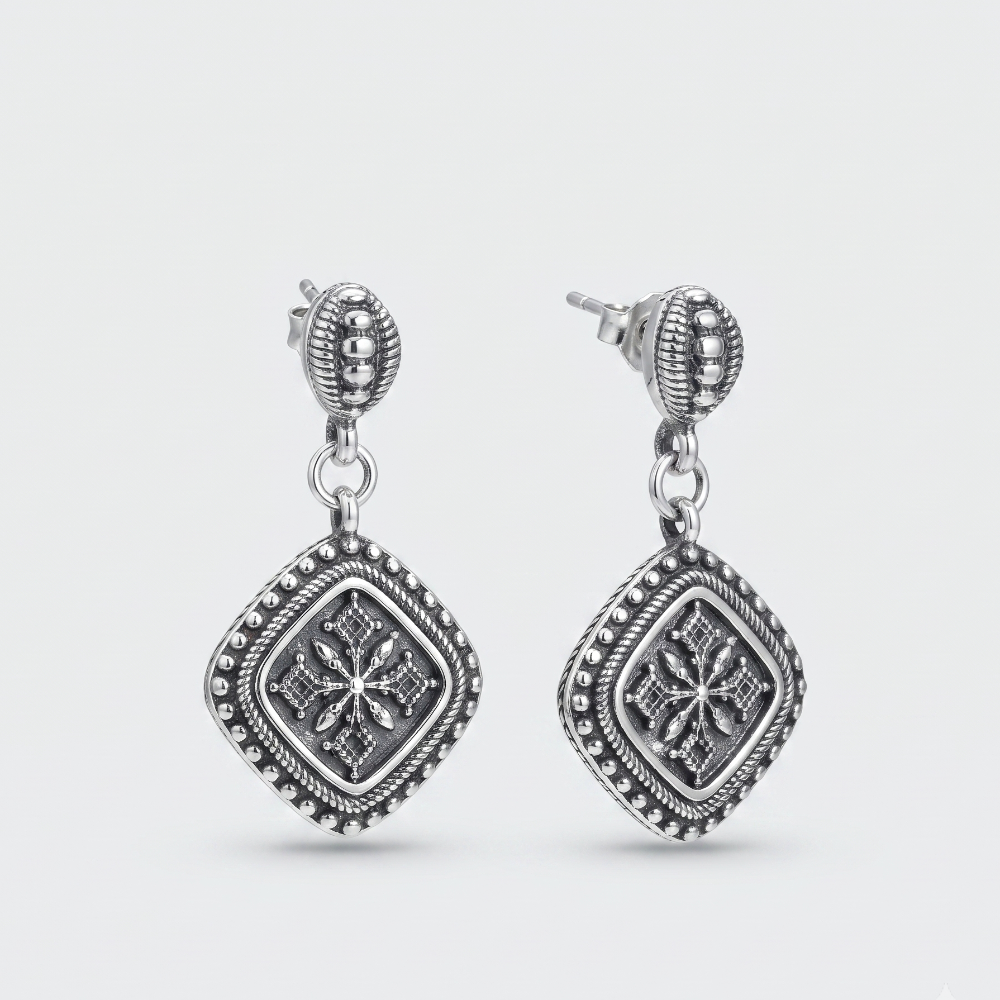 A pair of silver-toned dangle earrings with ornate filigree and beaded details, shown on a light gray background.
