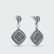 A pair of silver-toned dangle earrings with ornate filigree and beaded details, shown on a light gray background.