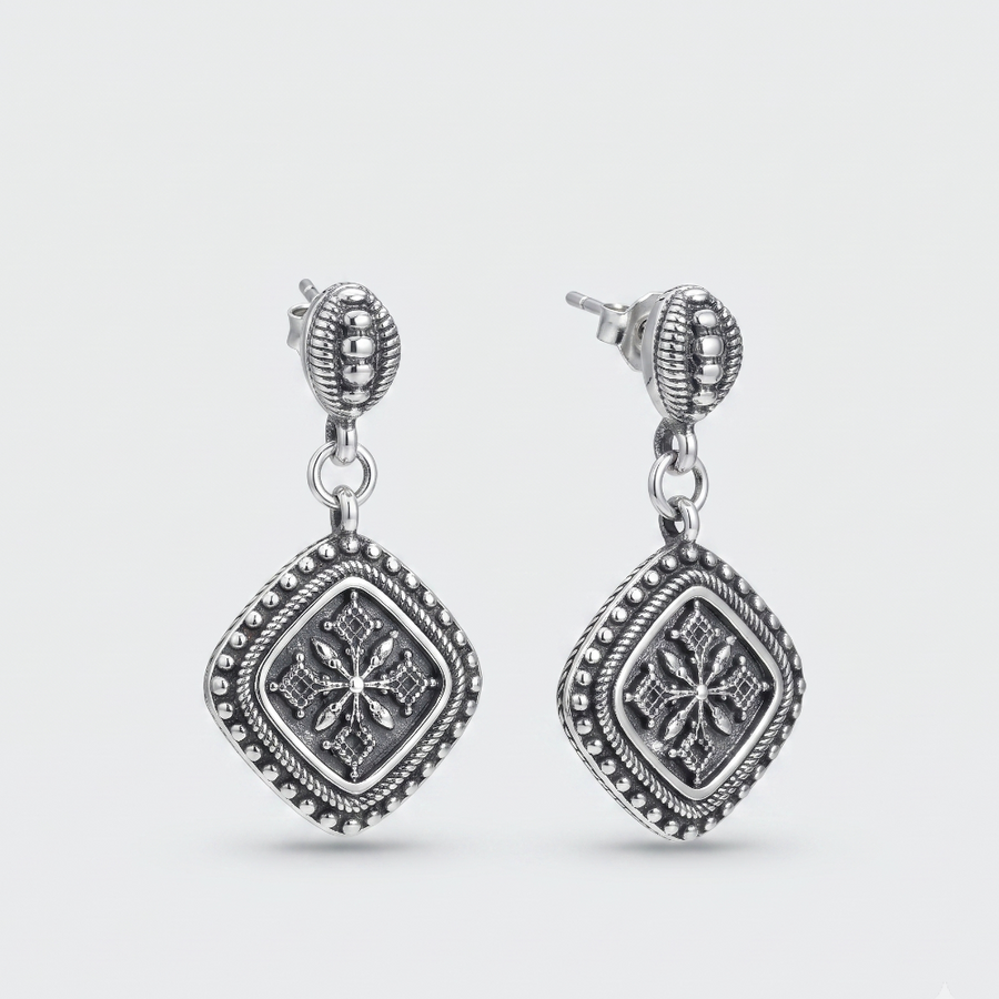 A pair of silver-toned dangle earrings with ornate filigree and beaded details, shown on a light gray background.