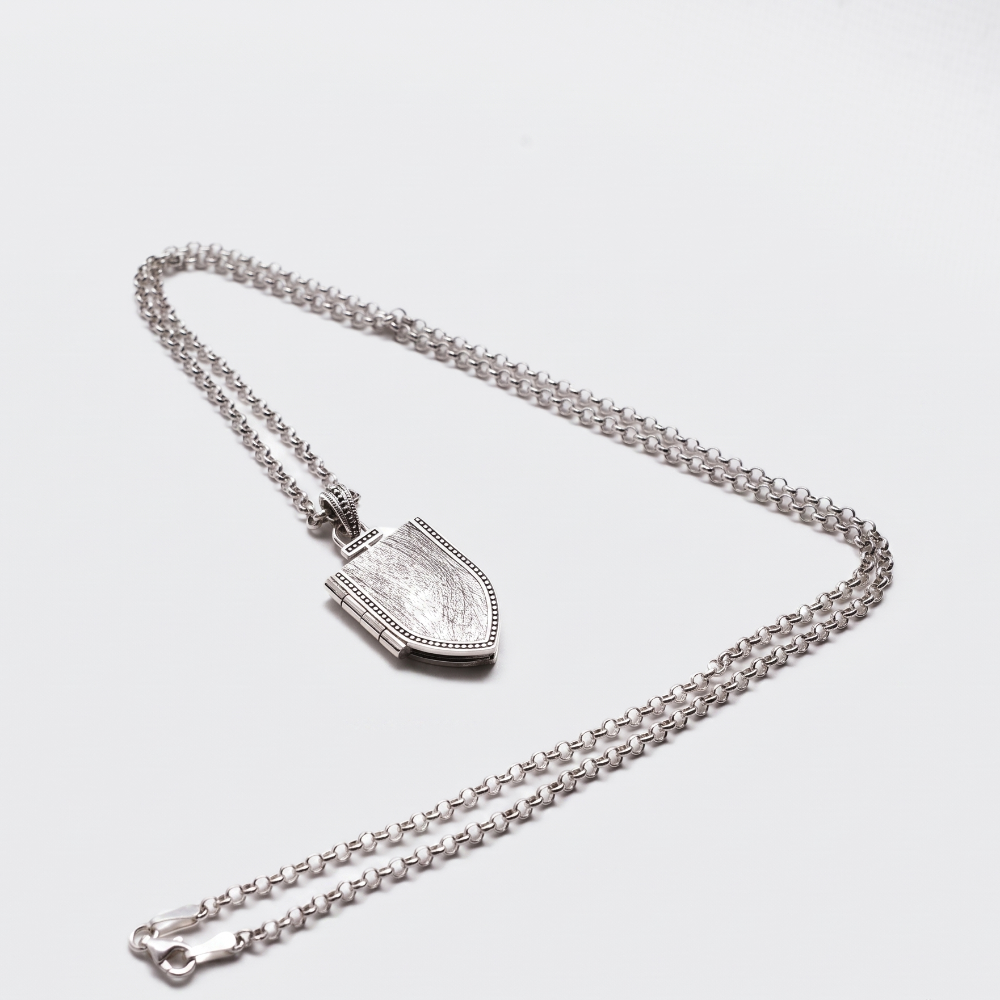 A silver-toned chain necklace with a shield-shaped pendant, displayed on a clean light gray background.