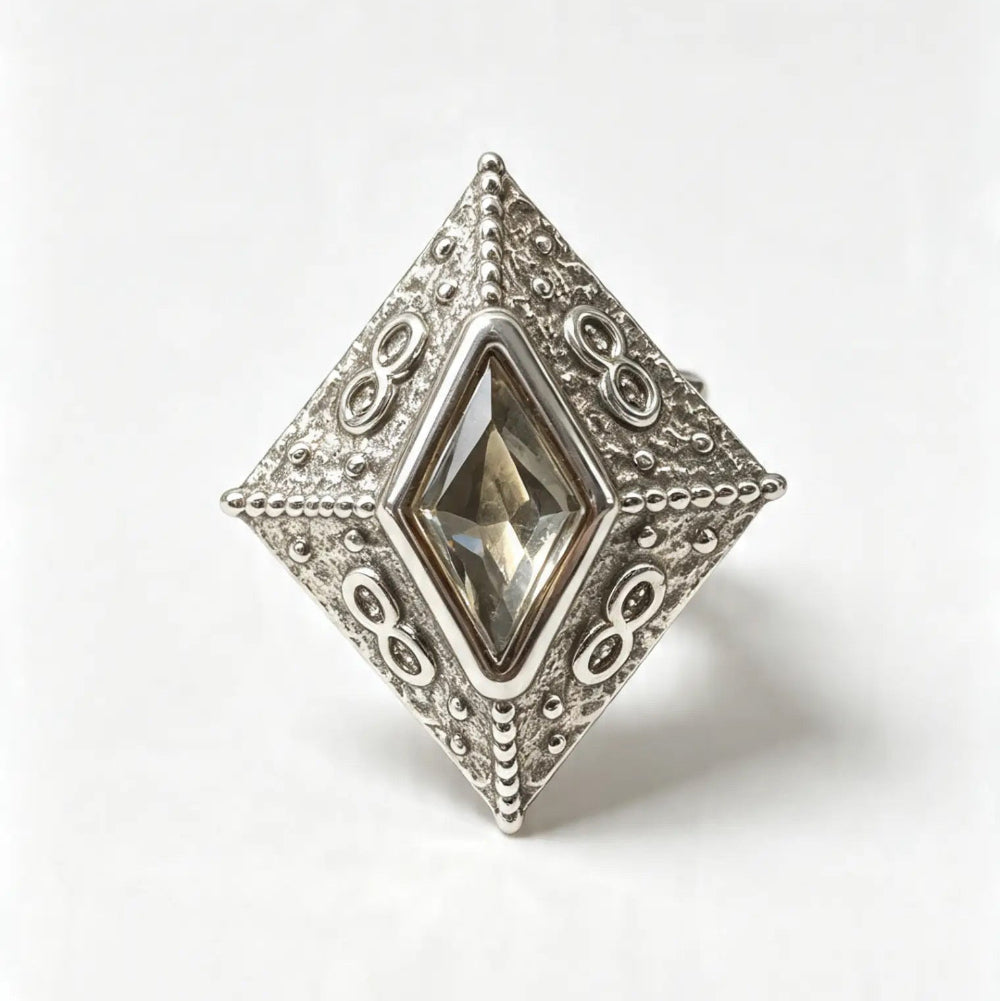A silver filigree ring with a large diamond-shaped clear gemstone, photographed on a clean white background.