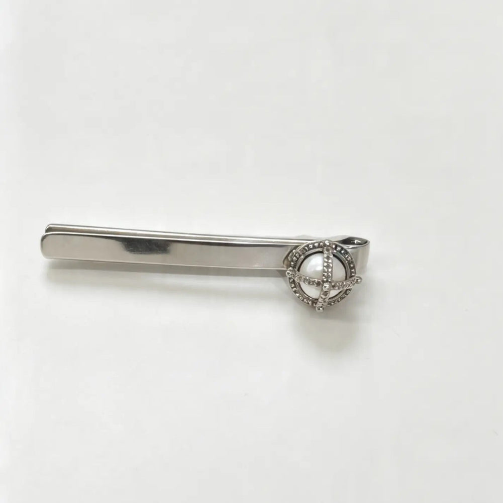 A silver-toned tie bar featuring a decorative oval heart-shaped centerpiece with a clear stone, set against a plain white background.
