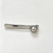 A silver-toned tie bar featuring a decorative oval heart-shaped centerpiece with a clear stone, set against a plain white background.