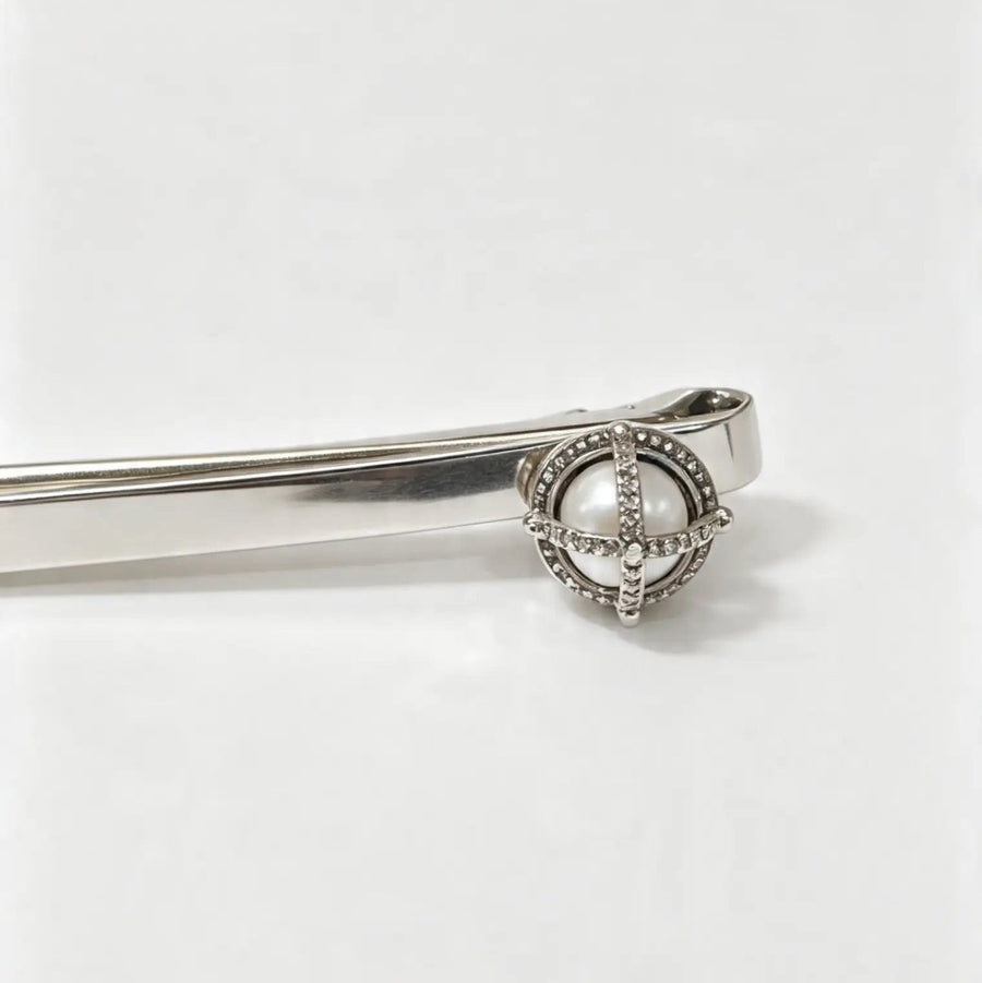 A silver-toned metal tie clip with a decorative circular head featuring a central white pearl and small clear stones, shown on a plain white background.