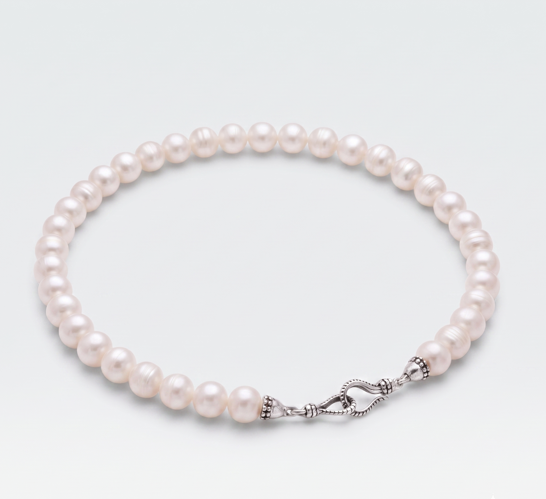 A strand of lustrous white freshwater pearls arranged in a circle with a silver-toned knotted clasp, photographed on a clean light gray background.