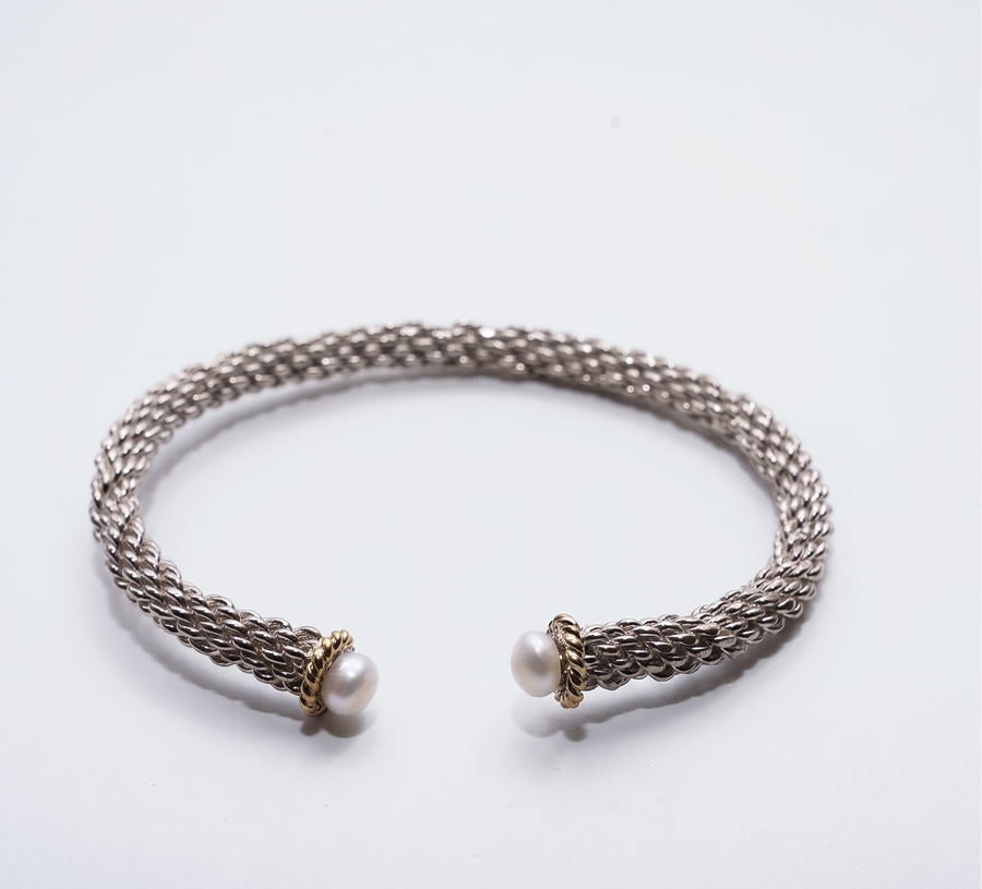 A silver-toned open cuff bracelet with a braided mesh texture and two small white pearl accents at the ends, set against a plain white background.