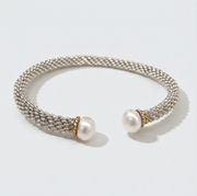 A silver-toned woven cuff bracelet with two white pearl ends and small gold-toned accents, photographed on a clean light gray background.