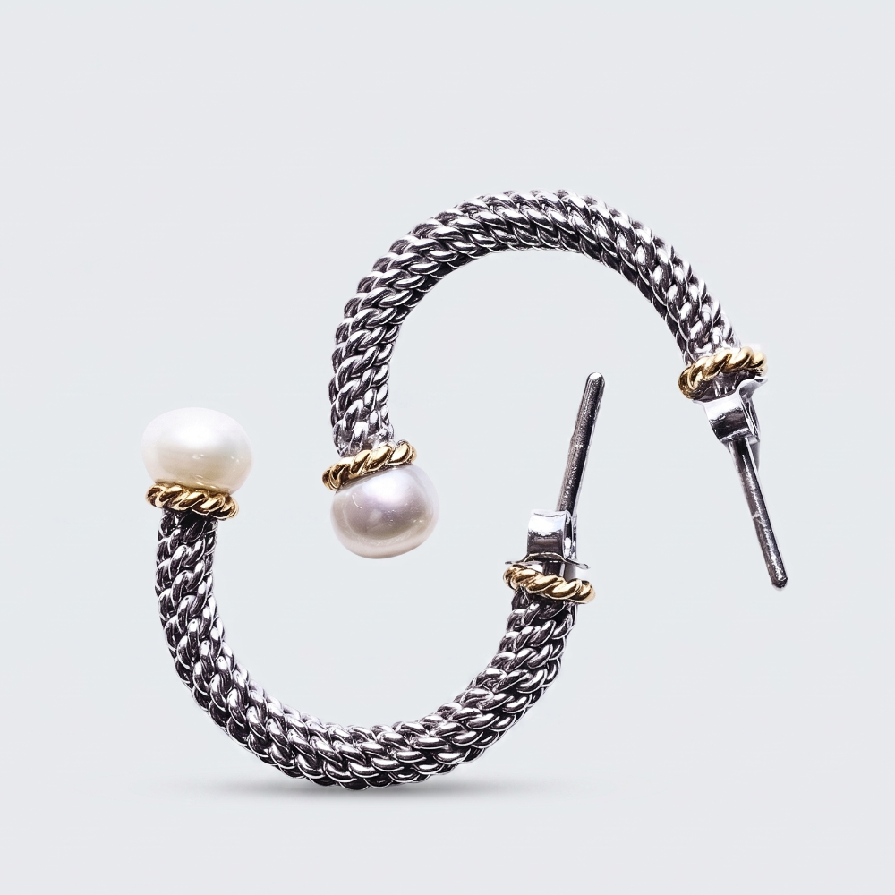 A silver-toned braided cuff bracelet with two white pearl beads and small gold-toned accent rings, shown on a light gray background.