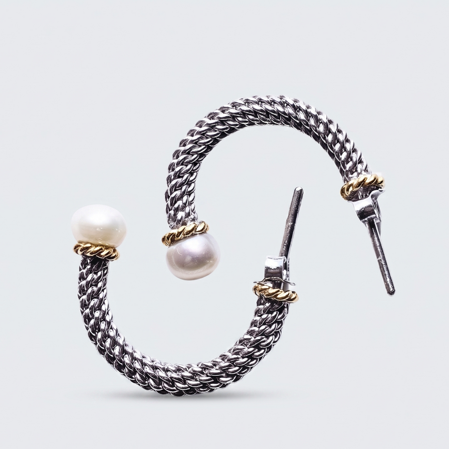 A silver-toned braided cuff bracelet with two white pearl beads and small gold-toned accent rings, shown on a light gray background.